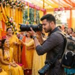 Indian wedding photographer shooting a candid haldi ceremony with a full-frame mirrorless camera and telephoto zoom lens